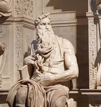 Moses statue seated with tablets, gripping his beard and looking upward.