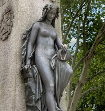 Mutter Kinzig statue with a leafy wreath, leaning against a stone monument and holding an overturned urn.