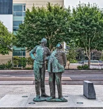 Two Working Men sculpture showing two weathered bronze figures standing side by side on a stone plinth, both looking upward to the left.