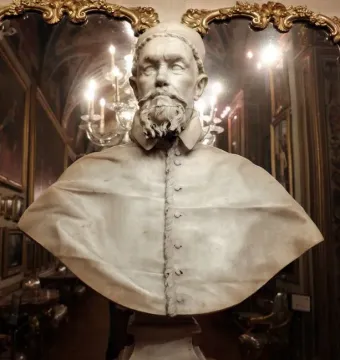 White marble bust of Pope Innocent X wearing a clerical cape and cap, displayed on a pedestal in an ornate room.
