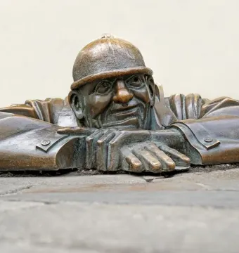 Čumil, a bronze man emerging from a street opening with his hands resting on the rim
