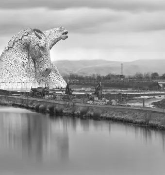 The Kelpies horse head sculptures beside calm water under a cloudy sky.