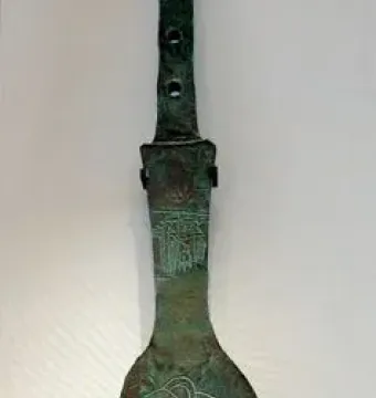 The Spear of Lugal, a tarnished metal artifact with an engraved feline figure and three holes in the handle.