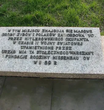 Granite memorial plaque for the Monument of Common Martyrdom with raised Polish lettering and two white candles beside it.