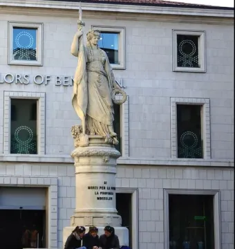 Monumento dell\'Indipendenza, a stone female statue holding a sword and wreath atop a tall pedestal with people seated on the steps below.
