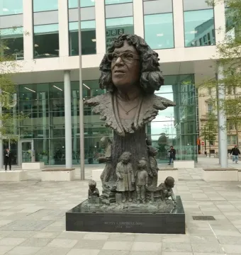 Betty Campbell statue showing a bronze bust of a bespectacled woman on a tall base, with small bronze figures and books around it.