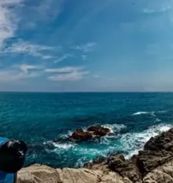 Coastal stone path beside the sea near Dona Marinera, with a person standing on the cliff overlooking the water.