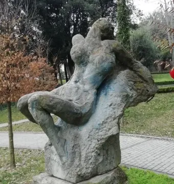Güzel İstanbul sculpture showing a gray, reclined stone figure in a grassy park near a paved path.