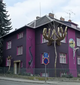 Kristek House in Brno with a dark purple facade, pink window accents, and surreal sculptural elements including large hands and a melting clock.