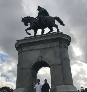 The Sam Houston Statue monument with a bronze rider on horseback above a stone archway, seen from below under a cloudy sky.