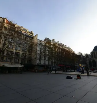 The Stravinsky Fountain with colorful abstract sculptures in a paved Paris square near historic buildings and a church.