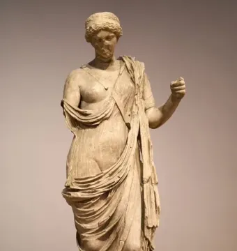 Armed Aphrodite marble statue on a dark pedestal, with a damaged face and missing left arm.