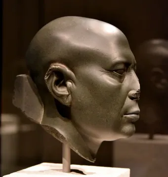 Berlin Green Head shown in right-side profile, a dark greenish-gray stone head with a worn nose and serious expression.