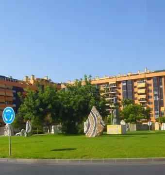 Dona Lluna sculpture on a bright yellow base in a grassy roundabout, with a crescent-shaped element at the top.
