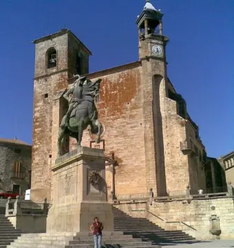 Francisco Pizarro equestrian statue on a stone pedestal in a cobbled square, with a historic stone building and tower behind it.