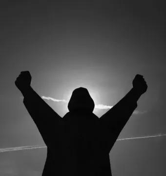 Silhouetted Monument to Stjepan Filipović with arms raised and fists clenched against a bright sky