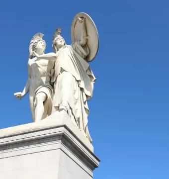 Athena Protects the Young Hero sculpture on a tall pedestal, showing two helmeted figures and a raised shield against the sky.