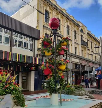 The Bucket Fountain sculpture in a light blue basin, decorated with colorful flower-filled buckets and a red sphere on top.