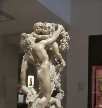 Faun Teased by Children marble sculpture with a muscular faun surrounded by cherubic children, grapes, and vines in a museum gallery.