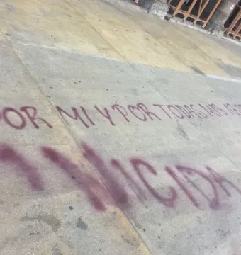Spanish graffiti on a light-colored sidewalk reading \