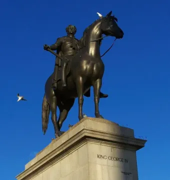 Equestrian Statue of George IV on a stone pedestal with a bronze horse and rider, against a blue sky with birds nearby.