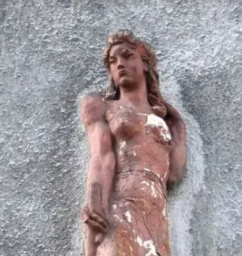 Weathered sculpture of a woman holding an oar against a grey wall.