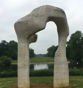 Henry Moore\'s The Arch stands on grass, framing water and distant trees under an overcast sky.