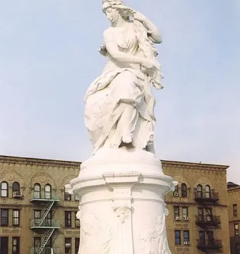 Lorelei Fountain with a seated female figure and smaller figures at the base in front of a brick apartment building.
