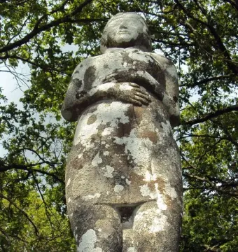 Vénus de Quinipily, a weathered stone statue covered in lichen and framed by tree branches.