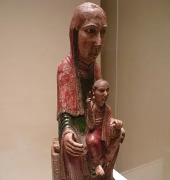 Virgin from Ger, an aged carved wooden figure of a woman holding a smaller figure on her lap, with faded red and green paint and a long veil.