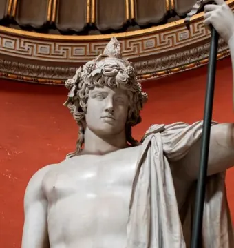 Marble statue of Antinous Braschi with a leaf and grape wreath, bare chest, draped cloth, and a staff against a red background.
