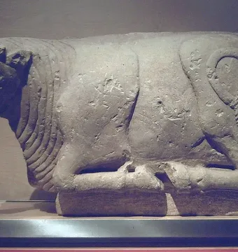 Light-colored stone Bull of Osuna sculpture shown in a recumbent pose with a detailed head and curled tail.