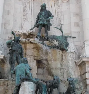 Fountain of King Matthias bronze sculpture showing a hunter with a fallen stag above figures and hunting dogs on rocky tiers.