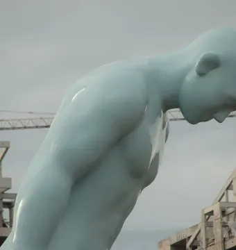 Greetingman sculpture with a pale blue figure bowing deeply under a cloudy sky.