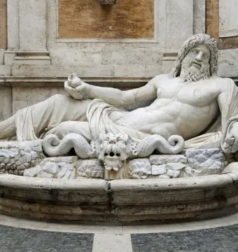 Marforio marble fountain statue reclining on a rocky base with a grotesque face spouting water below.