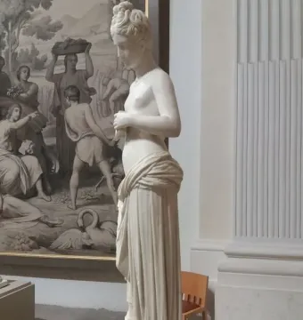 Pandora, a white marble neoclassical female statue with her head bowed and hands clasped in front of her torso.