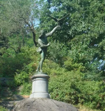 The Falconer bronze statue of a man releasing a bird of prey on a stone pedestal among green foliage.