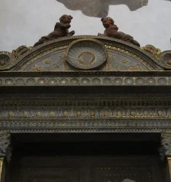 Ornate classical frame with gilded details and cherubic figures above a dark opening, from the Cavalcanti Annunciation.