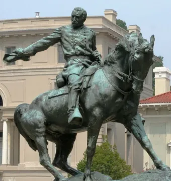 Weathered bronze equestrian statue of General Philip Sheridan with an outstretched arm, set against trees and classical buildings.