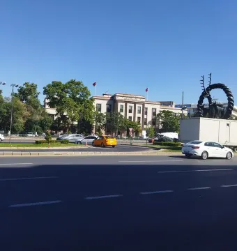 Hittite Sun Disk Monument on a white base in an urban street with cars and buildings in the background.