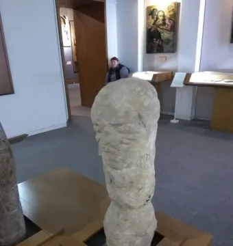 Škloŭ Idol stone sculpture displayed on a wooden stand in a museum gallery.