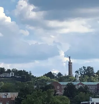 The Vulcan statue stands atop a tall stone column overlooking a cityscape from a wooded ridge.