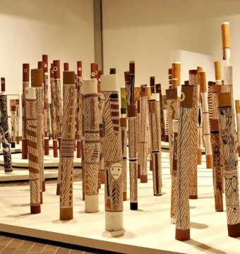 Aboriginal Memorial sculpture made up of numerous decorated wooden poles standing upright on a light-colored platform.