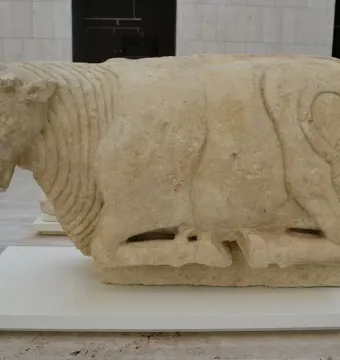 Bull of Osuna stone sculpture shown in profile on a white plinth.
