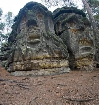 Devil\'s Heads sandstone carvings in a forest, showing two large stone faces on the outcrop.