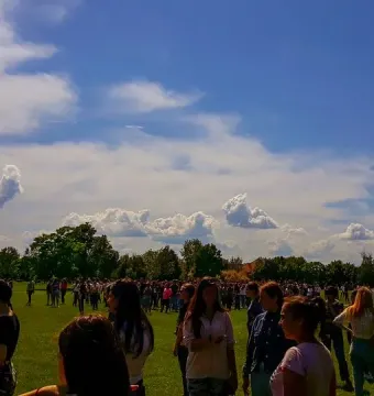 The Endless Column rises beside a green field under a blue sky with clouds, with many people gathered below.