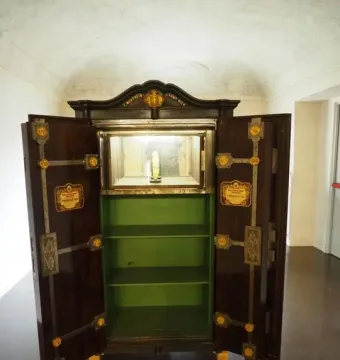 Venus of Chiozza displayed upright in a lit glass case inside an open wooden safe.