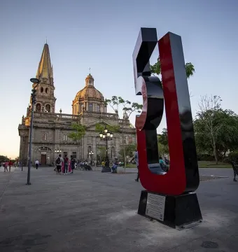 Antimonumento 5J standing on a paved plaza with a historic church and spires in the background.