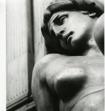 Reclining marble figure of Dawn with a downcast expression and bare shoulder and breast.