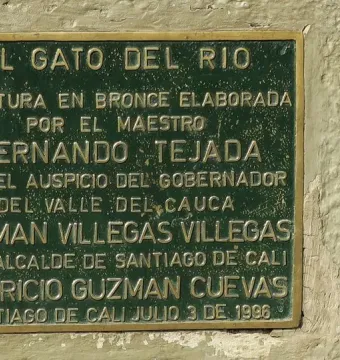 Green commemorative plaque with raised metal lettering mounted on a textured wall.